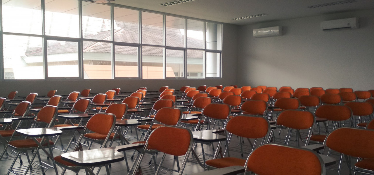 Bild von einem leeren großen Klassenzimmer mit Tischen und Stühlen.